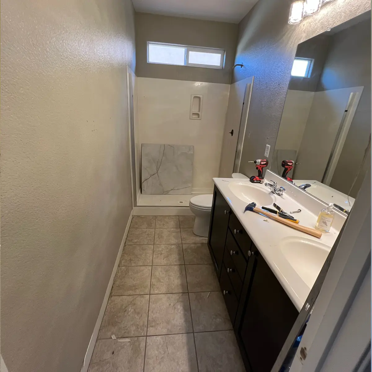 A double vanity painted black, tile flooring, and a walk-in shower in progress