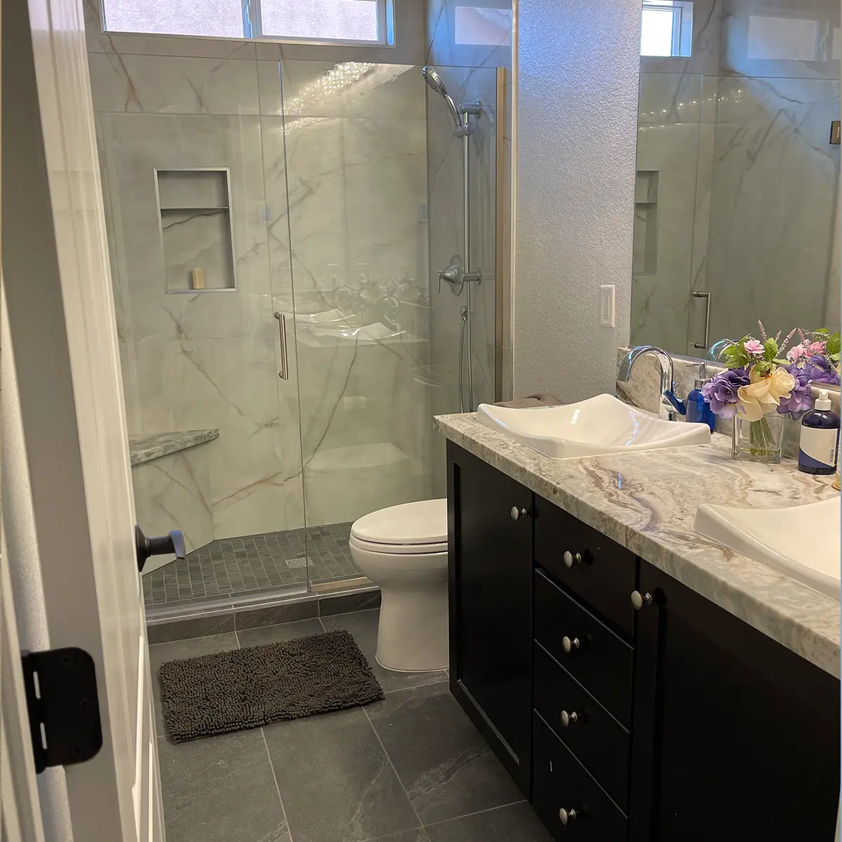 A small bathroom with tile flooring, quartz countertop, a walk-in shower, and two beautiful sinks