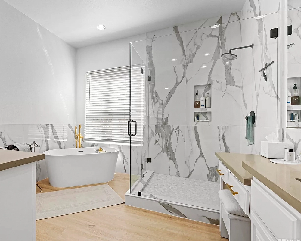 A bathroom with laminate flooring, glass walk-in shower, and small freestanding tub with golden fixtures