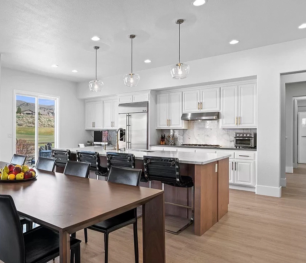 White kitchen cabinets with golden hardware, pendant and recessed lights, and a large kitchen island with quartz countertop