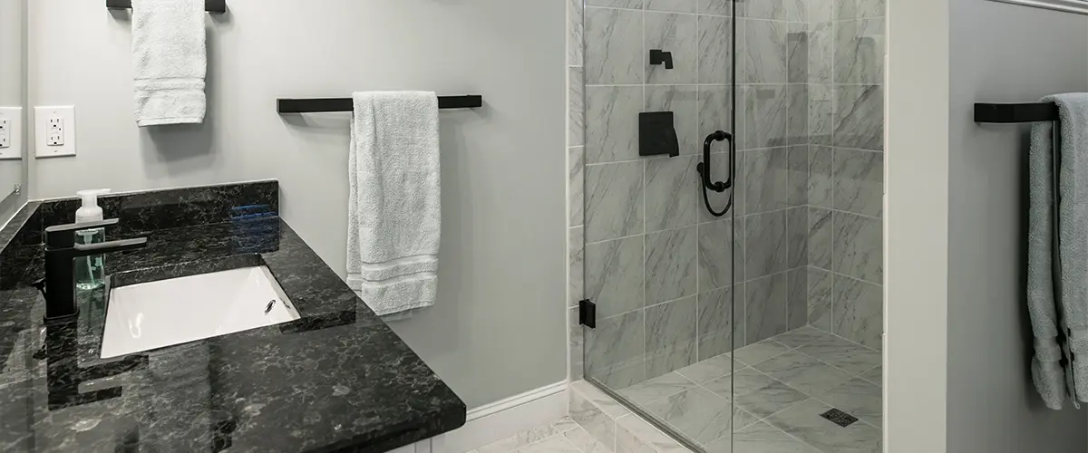 A black granite countertop with a glass shower with black hardware and water fixture