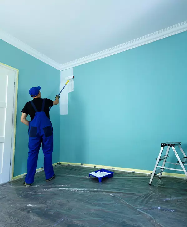 Man in a working overall is painting the wall in white color