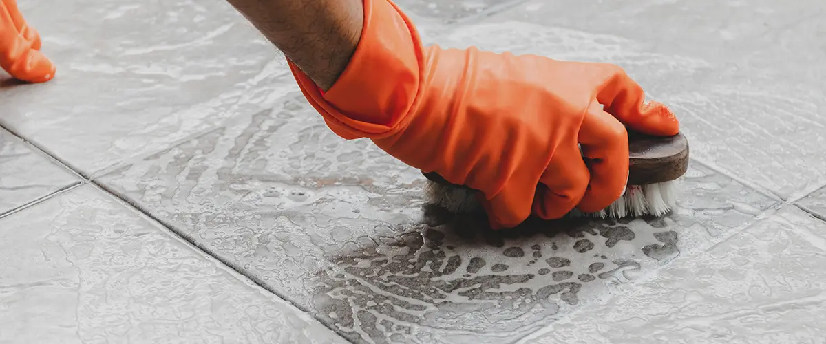 Hand of man wearing orange rubber gloves is used to scrub cleaning on the tile floor.