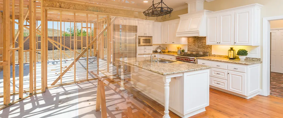 Composite image of a modern white kitchen with granite countertops overlaid with the wooden framing of a house under construction.