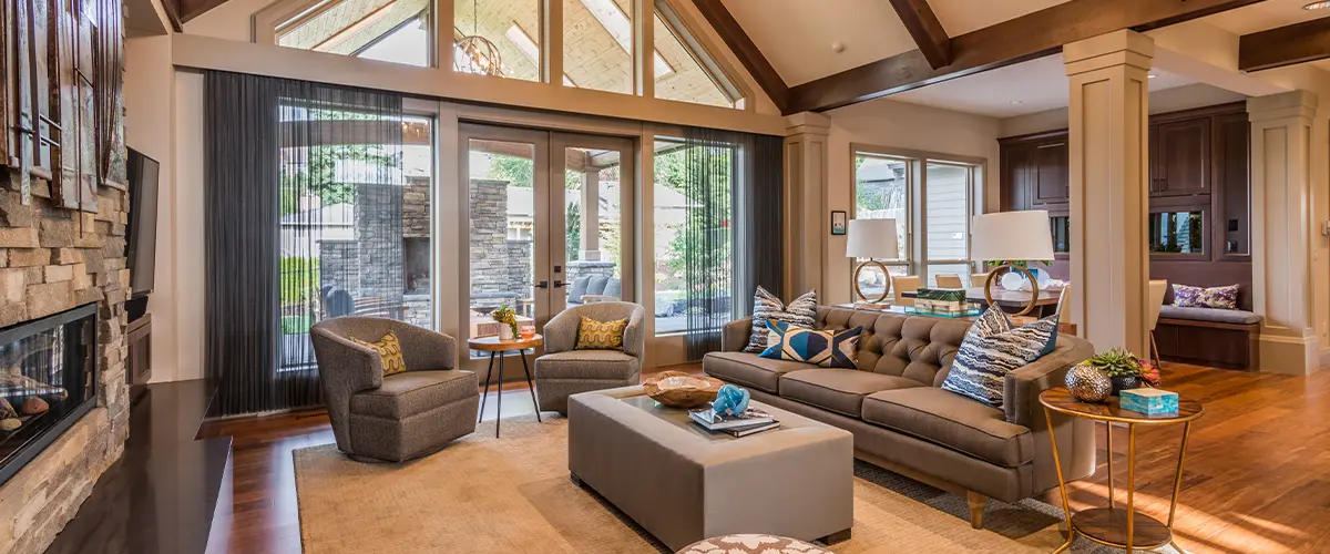 Elegant home remodeling in Sparks, with high vaulted ceilings and exposed wooden beams, featuring a stone fireplace, cozy seating, and large windows overlooking an outdoor patio.