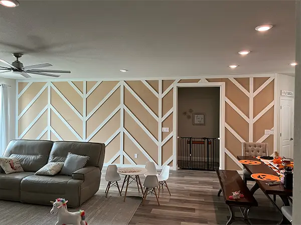 Modern home remodeling in Sparks, with living room with a unique accent wall featuring a geometric pattern of white trim on beige panels, a gray leather sofa, and a children's play area.