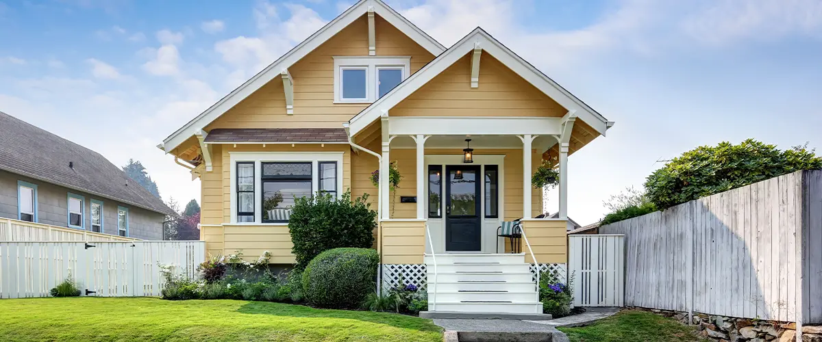 Yellow Craftsman-style house with manicured lawn, white picket fence, and inviting front porch, showcasing exterior painting in Renol