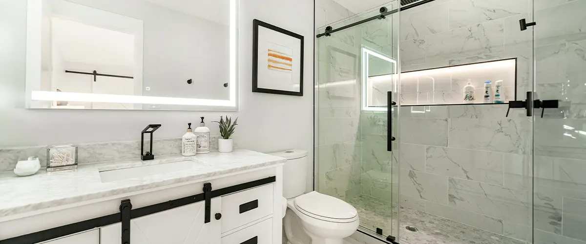 Modern bathroom with illuminated vanity mirror, glass semi-frameless shower doors, and marble countertop - contemporary bathroom design and renovation.