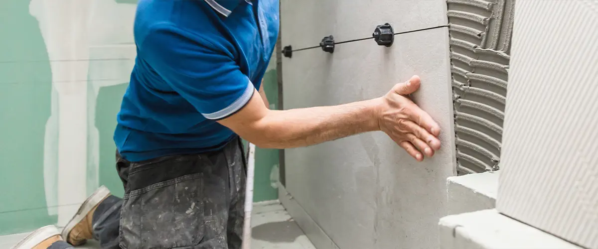 Worker installing large ceramic tiles on a wall using adhesive in a shower remodeling project in Reno.