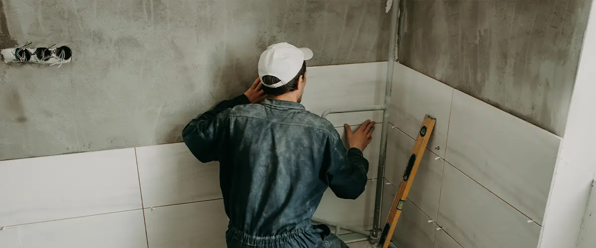 Contractor carefully installing white ceramic tiles on a bathroom wall during a bathroom remodeling project.