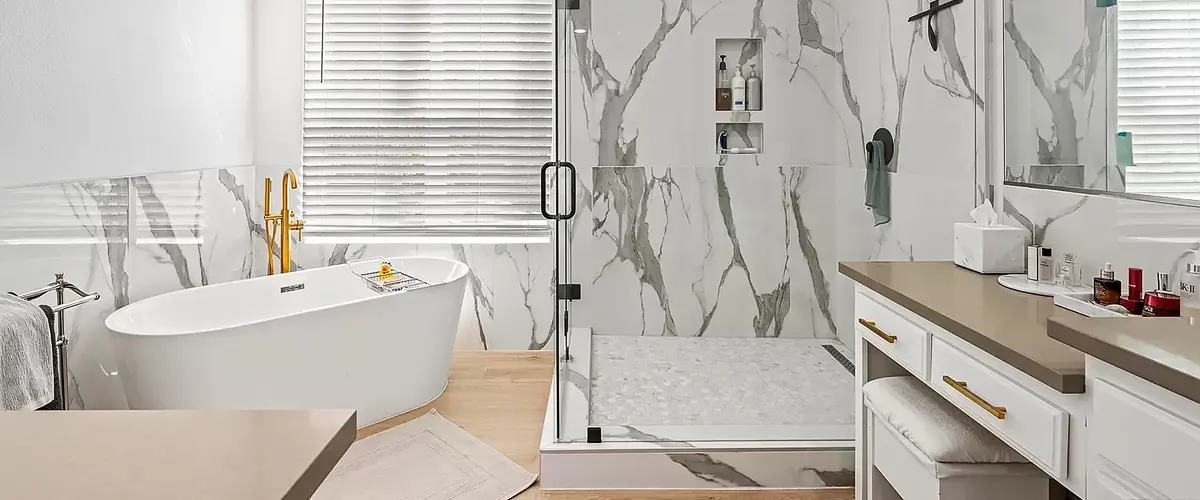 Modern bathroom featuring a marble-tiled shower, standalone bathtub, and vanity with gold accents.