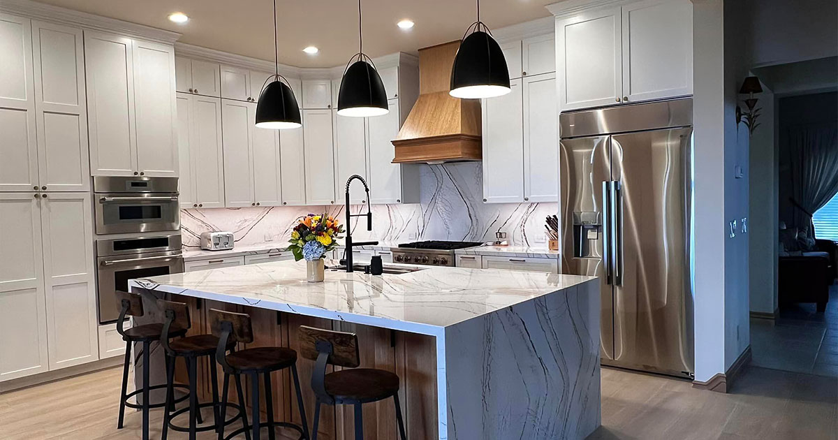 Modern kitchen with white cabinets, stainless steel appliances, and a large marble island with pendant lights.