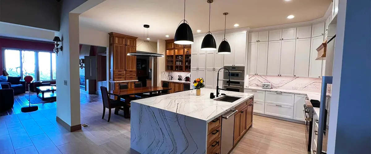 Modern kitchen with white cabinets, stainless steel appliances, and a large marble island with pendant lights.