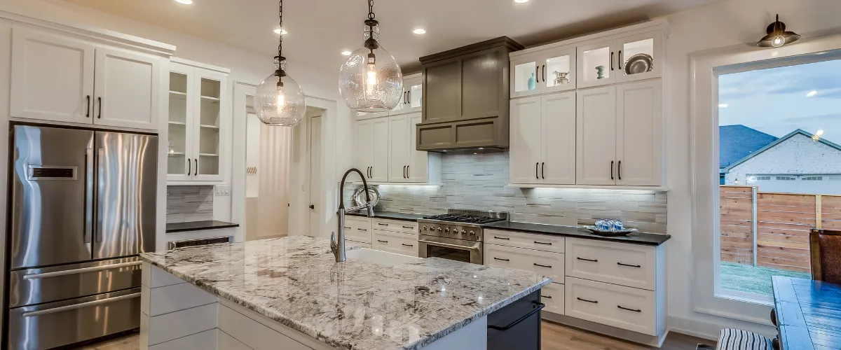 A luxurious kitchen with a granite island, pendant lights, and a combination of white and dark cabinetry, blending modern and traditional styles.